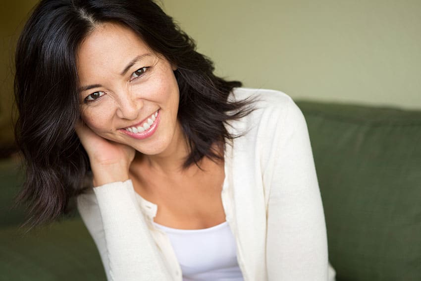 woman showing off her healthy smile, sitting on her couch at home